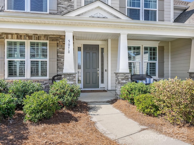 doorway to property featuring a porch, roof with shingles, and stone siding