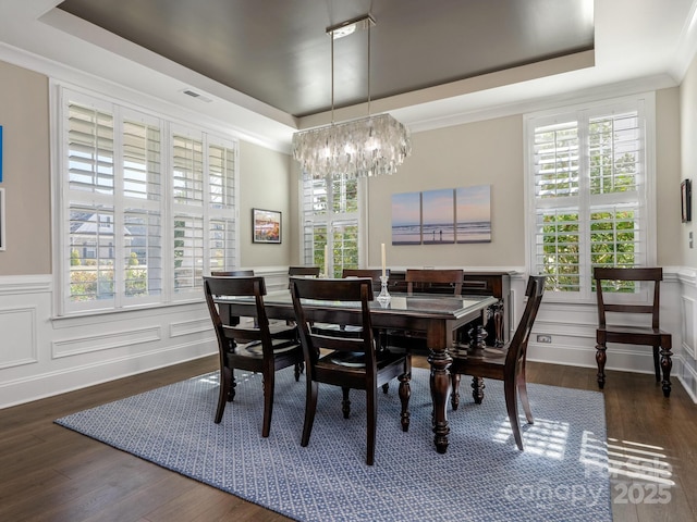 dining room with a decorative wall, a raised ceiling, a chandelier, and wood finished floors