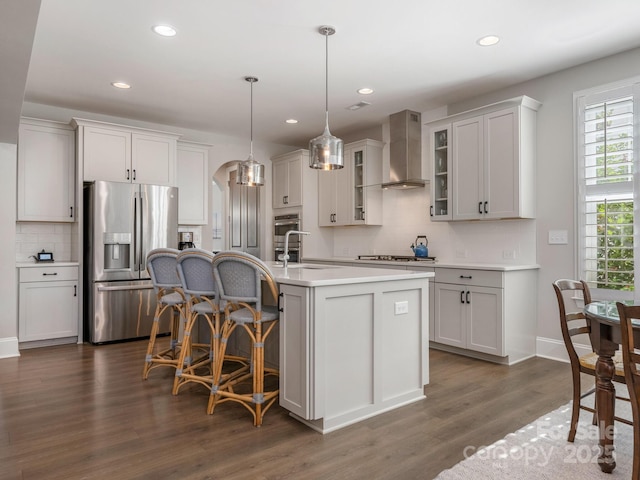 kitchen with tasteful backsplash, wall chimney range hood, light countertops, appliances with stainless steel finishes, and a kitchen bar