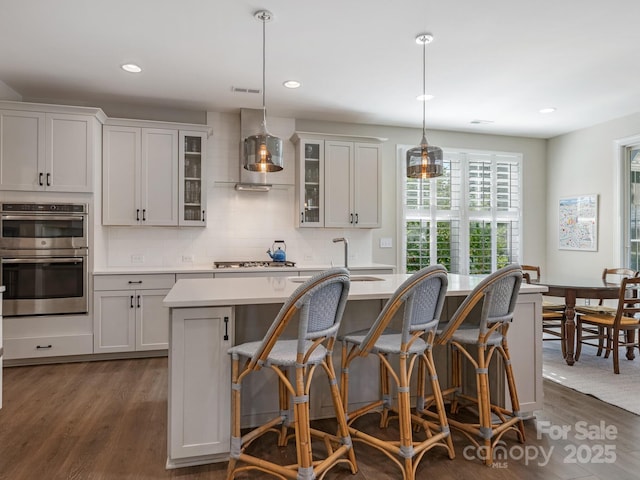 kitchen featuring light countertops, a breakfast bar, a kitchen island with sink, dark wood finished floors, and stainless steel appliances