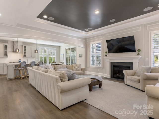 living room with recessed lighting, a fireplace with flush hearth, a tray ceiling, and wood finished floors