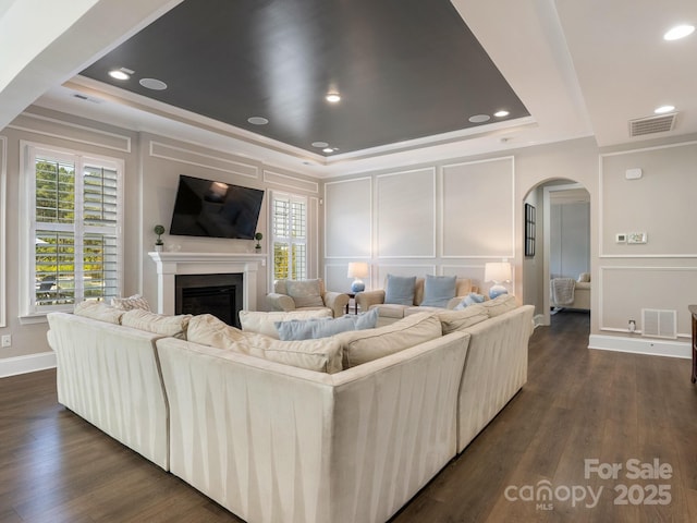 living room with a raised ceiling, arched walkways, a decorative wall, and visible vents