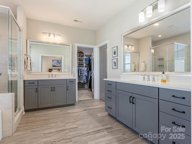 bathroom featuring visible vents, a sink, a wealth of natural light, wood finished floors, and a stall shower