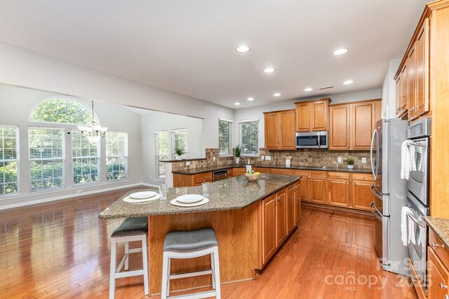 6941 Augustine Way, Charlotte, NC 28270 - kitchen featuring stainless steel appliances, brown cabinetry, light wood-style flooring, tasteful backsplash, and a breakfast bar