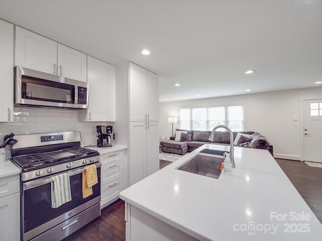 kitchen with dark wood-style floors, a sink, open floor plan, light countertops, and appliances with stainless steel finishes