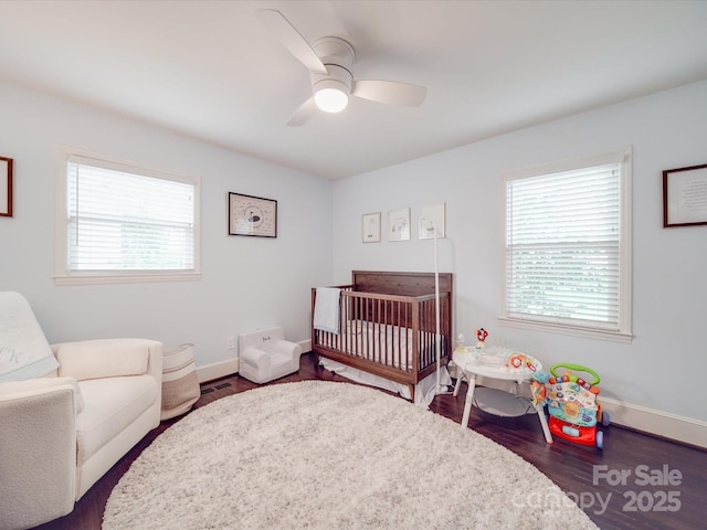 bedroom with a nursery area, baseboards, wood finished floors, and ceiling fan