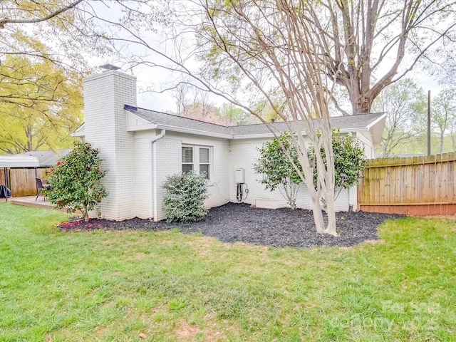 exterior space with brick siding, a yard, a chimney, and fence