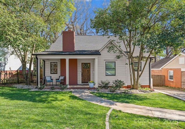 view of front of home with fence, a front yard, a shingled roof, and covered porch