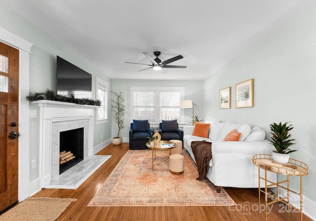 living area with baseboards, a ceiling fan, wood finished floors, and a tiled fireplace