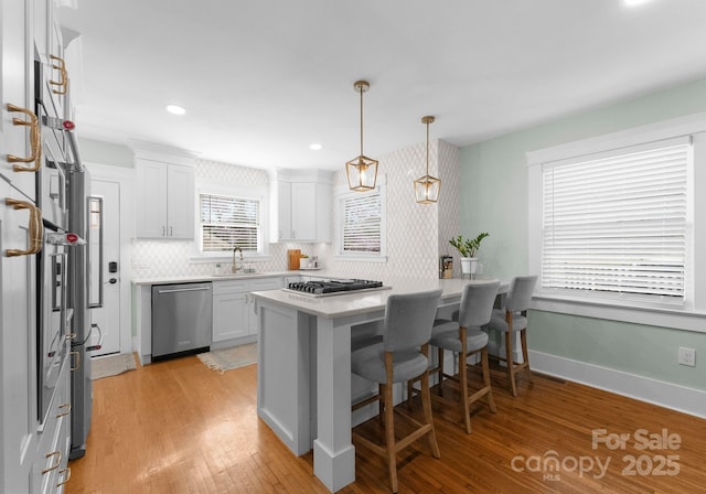 kitchen featuring a kitchen breakfast bar, light wood-type flooring, stainless steel appliances, light countertops, and white cabinetry