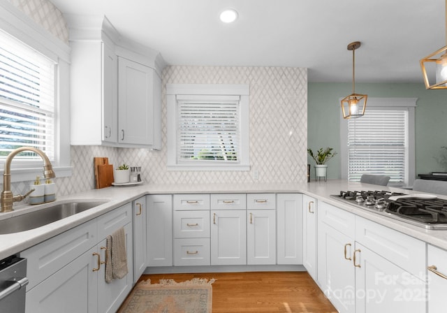 kitchen featuring white cabinets, light wood-style flooring, a sink, light countertops, and appliances with stainless steel finishes