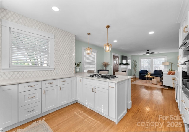 kitchen with a ceiling fan, stainless steel gas cooktop, a fireplace, light wood-style flooring, and white cabinets
