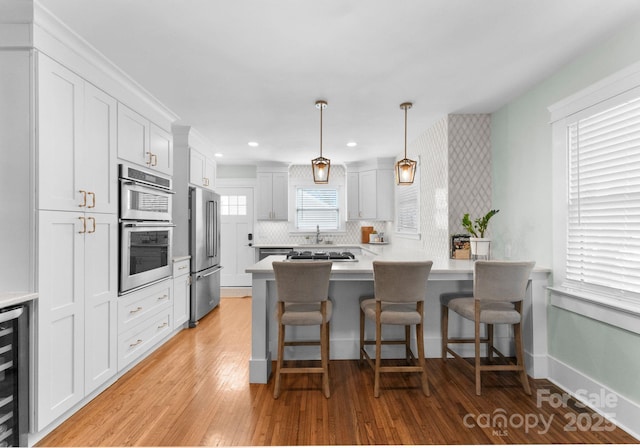 kitchen featuring a kitchen breakfast bar, light wood-type flooring, stainless steel appliances, light countertops, and white cabinets