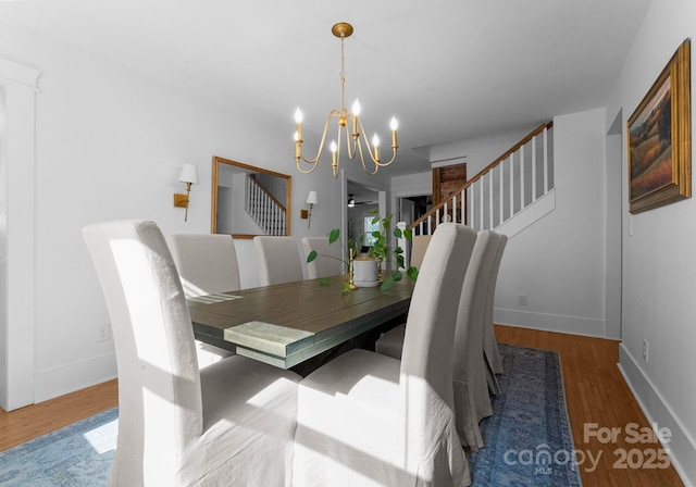 dining space with stairway, wood finished floors, baseboards, and a notable chandelier