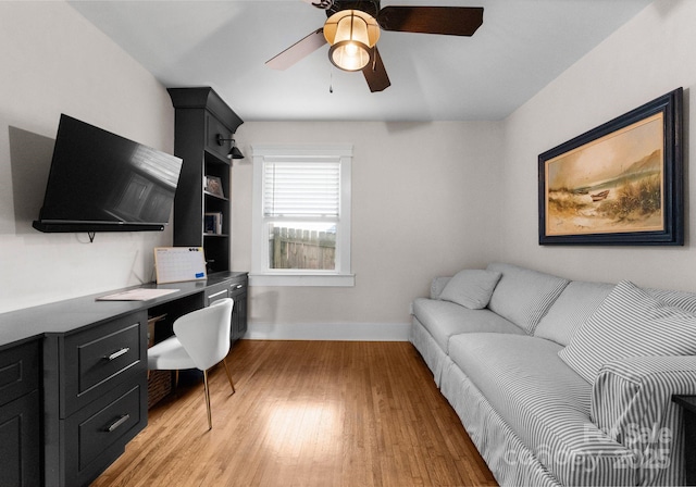 office space with light wood-style flooring, baseboards, ceiling fan, and built in study area