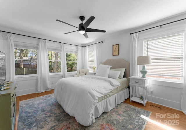 bedroom with wood finished floors, a ceiling fan, baseboards, and multiple windows