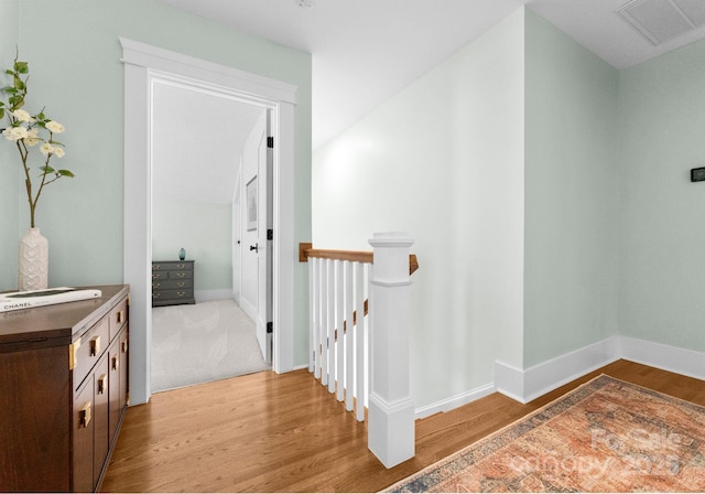 hall featuring wood finished floors, visible vents, baseboards, and an upstairs landing