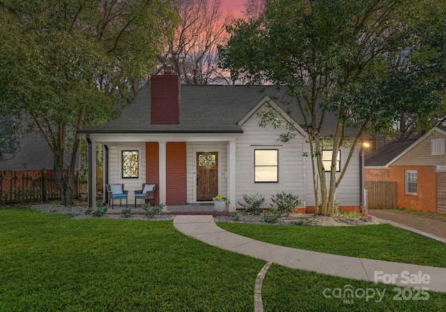 view of front of home with a porch, a lawn, fence, and roof with shingles