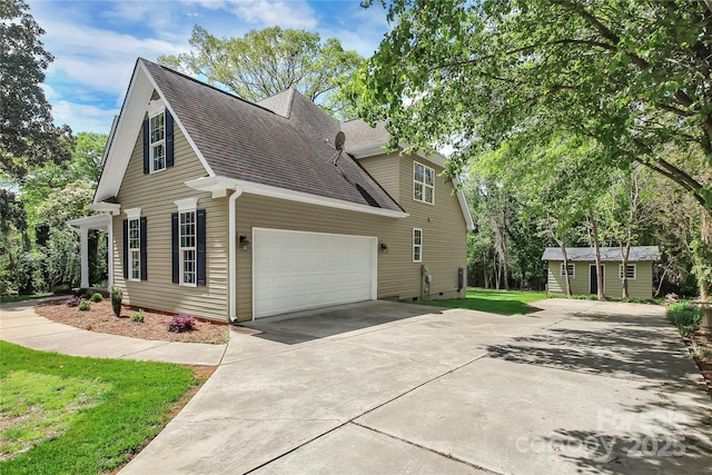 view of side of property with a shingled roof, a lawn, and concrete driveway