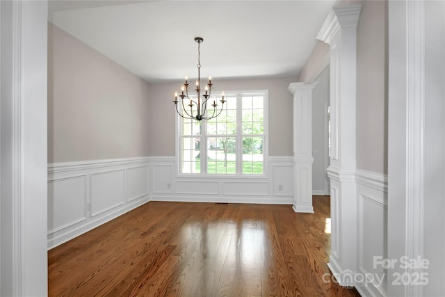 unfurnished dining area featuring a decorative wall, a notable chandelier, a wainscoted wall, and dark wood-style floors
