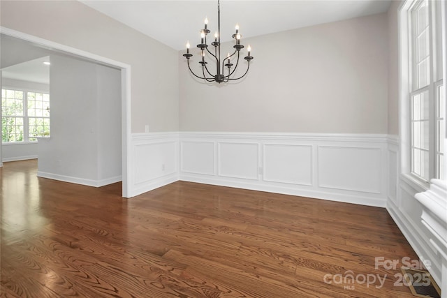 spare room with wainscoting, dark wood-style flooring, and an inviting chandelier