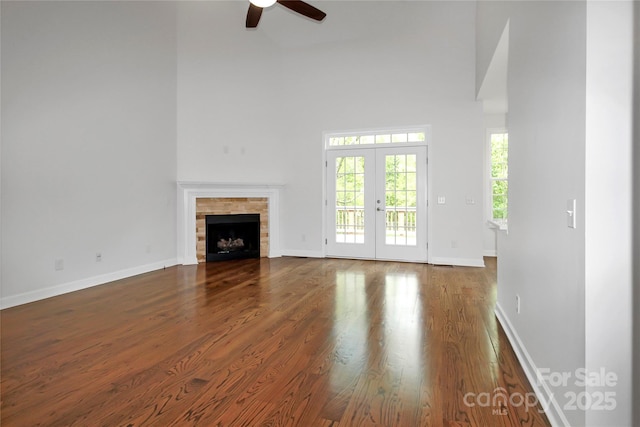 unfurnished living room featuring a towering ceiling, a ceiling fan, wood finished floors, french doors, and baseboards