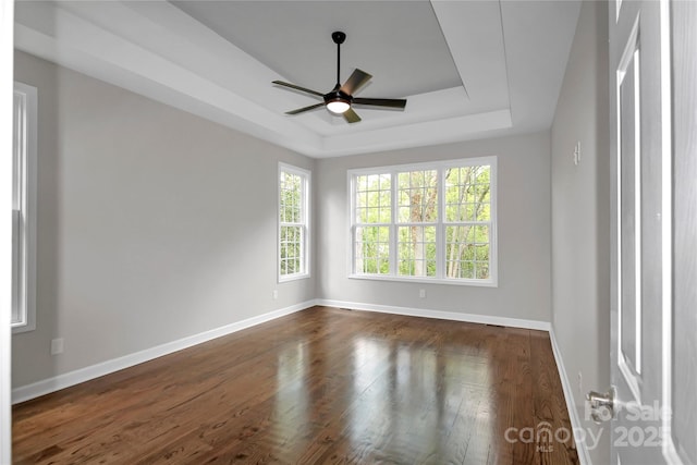 spare room with a tray ceiling, dark wood finished floors, baseboards, and a ceiling fan