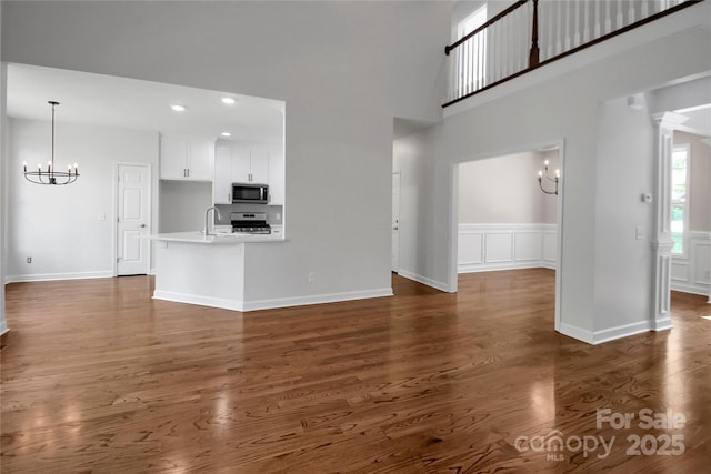 unfurnished living room featuring a wainscoted wall, a chandelier, recessed lighting, a sink, and dark wood-style floors