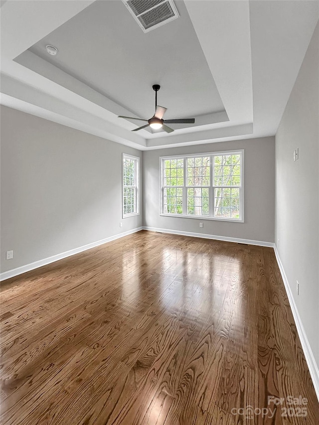 unfurnished room with visible vents, baseboards, ceiling fan, a tray ceiling, and wood finished floors