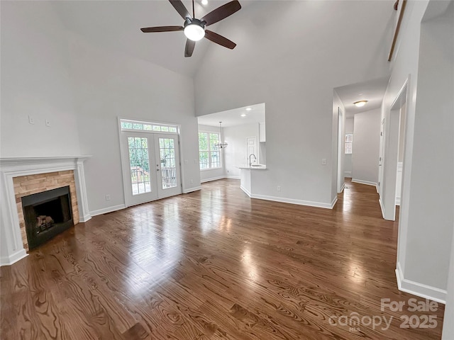 unfurnished living room with dark wood-style flooring, baseboards, a fireplace, ceiling fan, and high vaulted ceiling