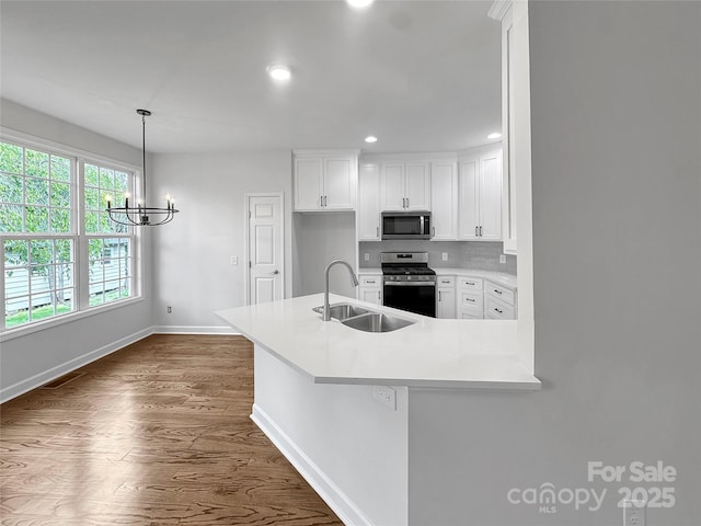 kitchen featuring white cabinetry, appliances with stainless steel finishes, a sink, baseboards, and a notable chandelier