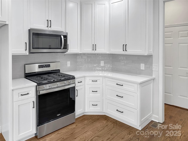 kitchen with stainless steel appliances, white cabinets, light countertops, and wood finished floors