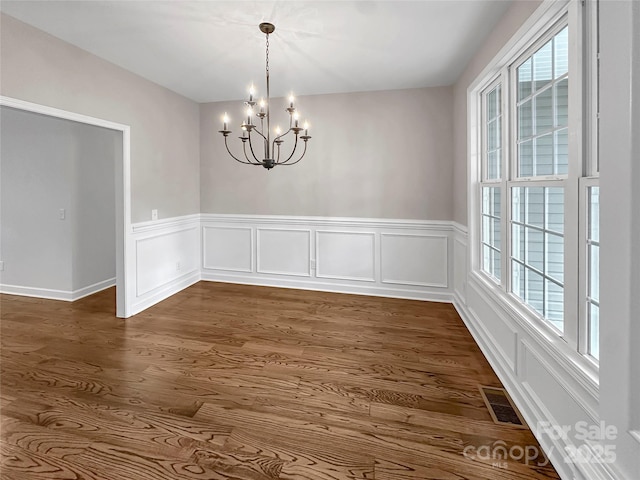 unfurnished dining area featuring wainscoting, an inviting chandelier, dark wood finished floors, and visible vents