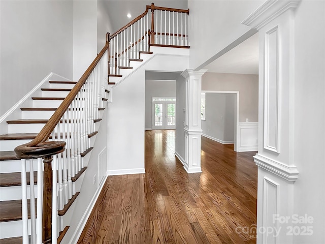 staircase featuring a towering ceiling, ornate columns, and wood finished floors
