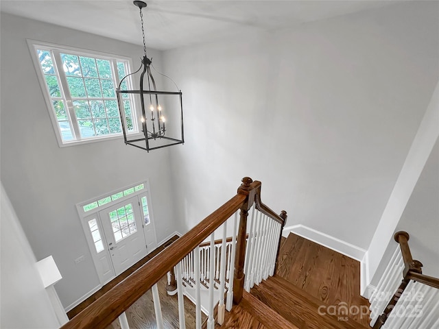 stairway featuring baseboards, an inviting chandelier, and wood finished floors