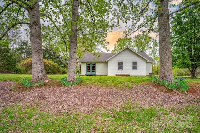 rear view of property with french doors, a shingled roof, and a lawn