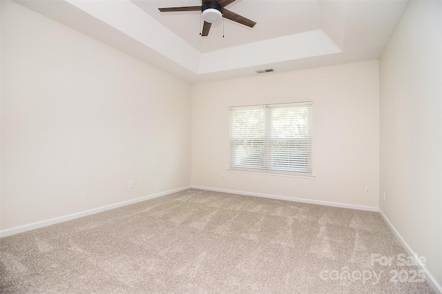 empty room featuring ceiling fan, visible vents, light carpet, and a tray ceiling