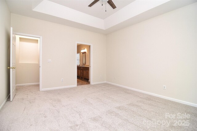 unfurnished bedroom featuring a raised ceiling, baseboards, ensuite bathroom, and light colored carpet