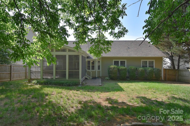 back of house with a fenced backyard, a lawn, a sunroom, and roof with shingles
