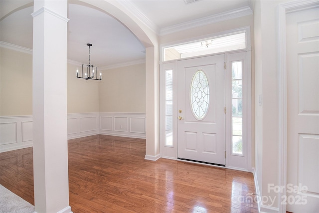 entrance foyer featuring crown molding, arched walkways, wainscoting, wood finished floors, and a notable chandelier