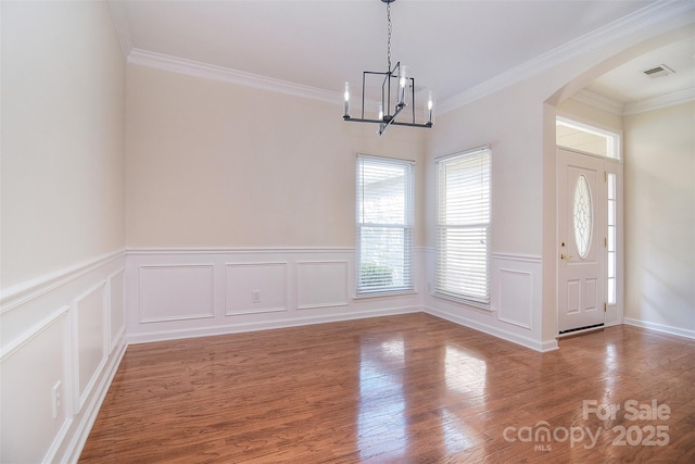 unfurnished dining area with crown molding, wainscoting, wood finished floors, a chandelier, and arched walkways