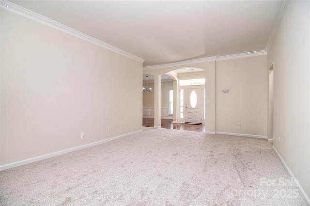 carpeted spare room featuring baseboards, arched walkways, ornate columns, and ornamental molding