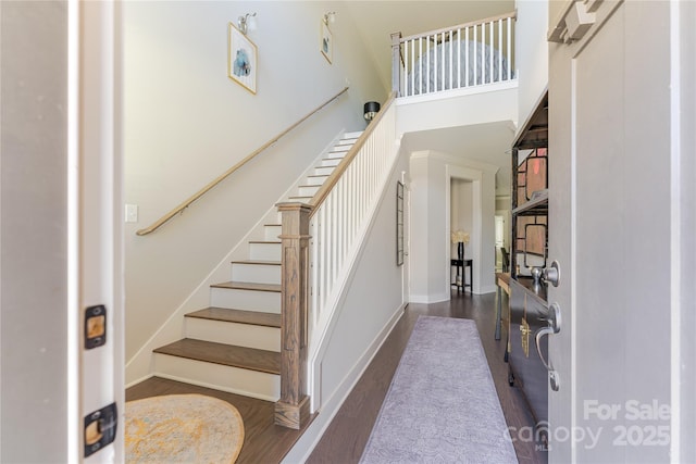 entryway featuring wood finished floors, a high ceiling, baseboards, and stairs