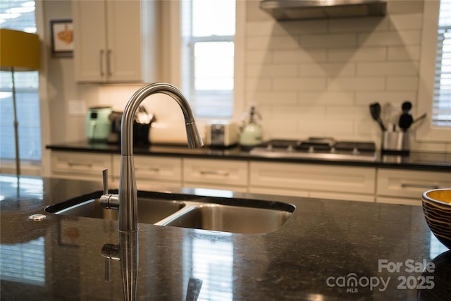 kitchen with decorative backsplash, ventilation hood, a sink, and white cabinetry