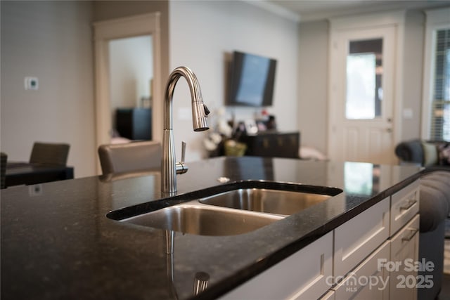 kitchen with dark stone counters, white cabinetry, and a sink