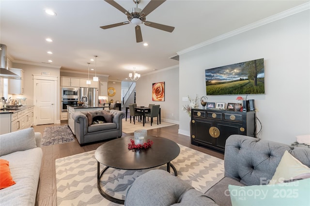 living room featuring stairway, wood finished floors, ceiling fan with notable chandelier, ornamental molding, and recessed lighting