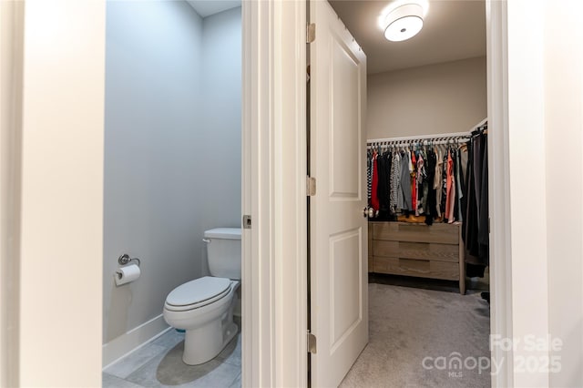bathroom with baseboards, a spacious closet, and toilet