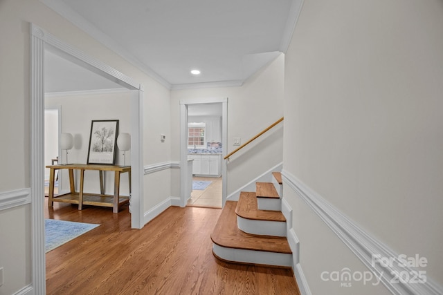 hallway featuring light wood finished floors, baseboards, stairway, and ornamental molding