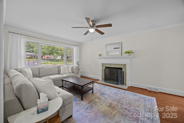 living area featuring wood finished floors, ceiling fan, a fireplace, baseboards, and visible vents