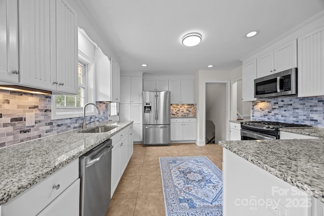 kitchen with a sink, tasteful backsplash, appliances with stainless steel finishes, light stone countertops, and light tile patterned floors